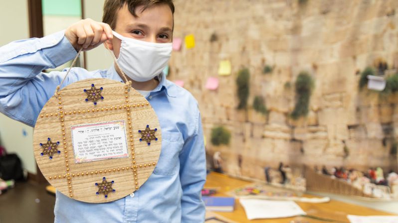 Young boy at school holding up art project.