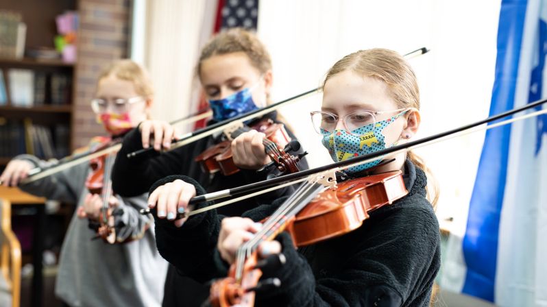 Young female students in masks playing violins.