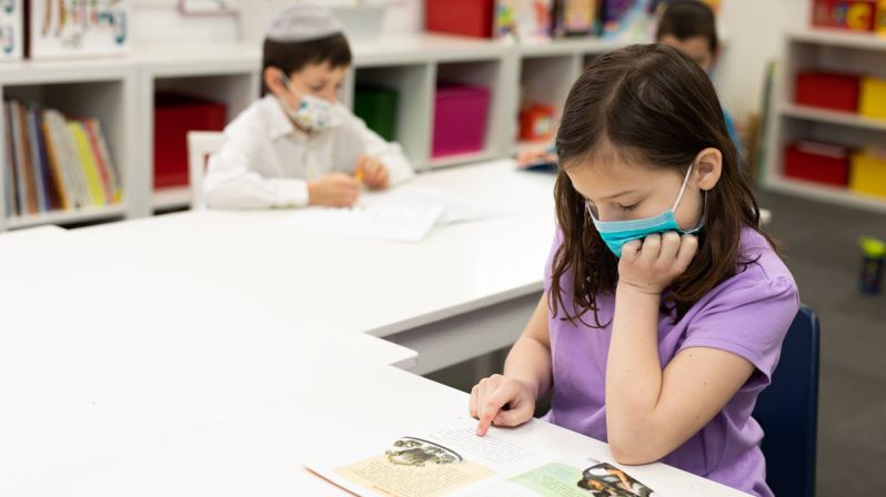 Young girl reading with other students in background.